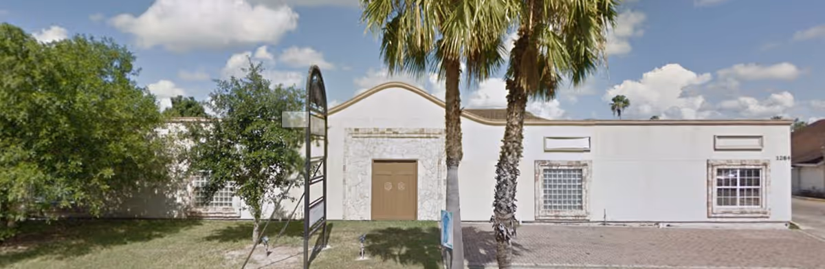Front exterior of a single-story facility with palm trees and a driveway.
