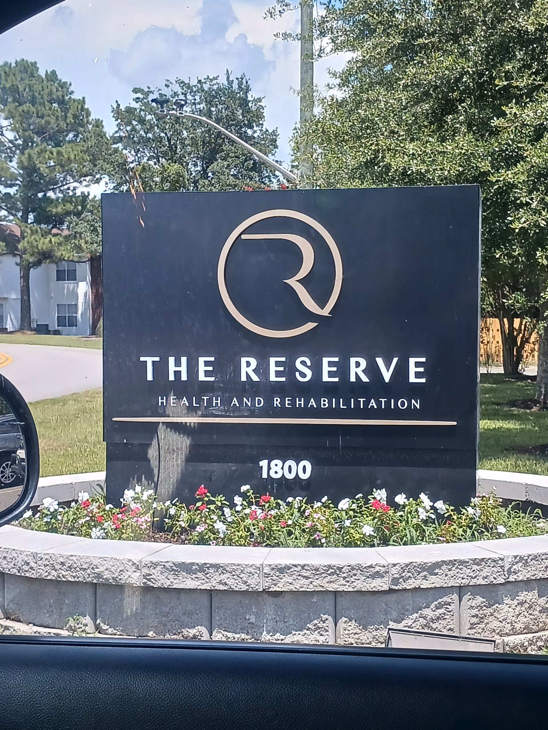 A dark exterior sign for The Reserve Health and Rehabilitation with flowers.