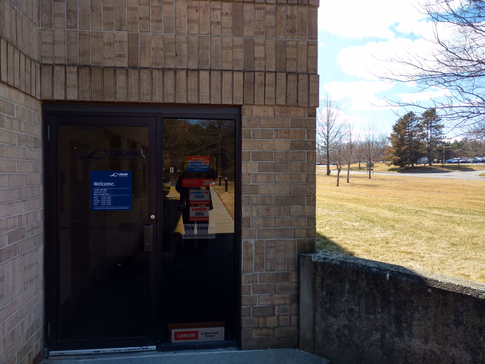 Glass door entrance with LinCare sign, brick exterior and grassy outdoor area.