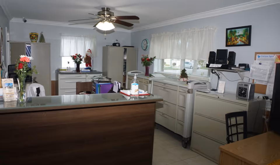 An interior reception/office area with a front desk, filing cabinets, ceiling fan, and windows with curtains.