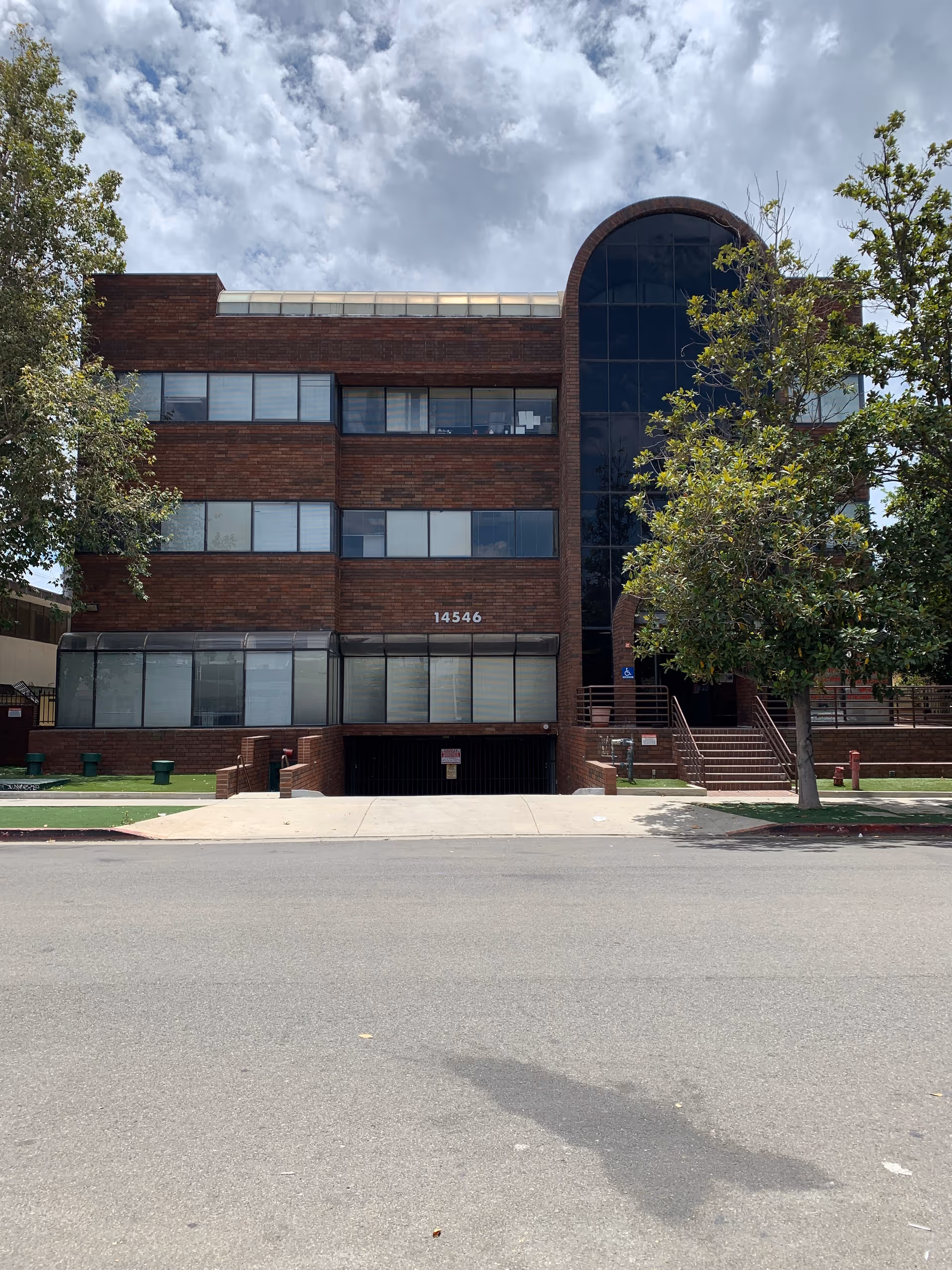 Brick multi-story building with curved glass entrance, trees flanking a street-facing front facade