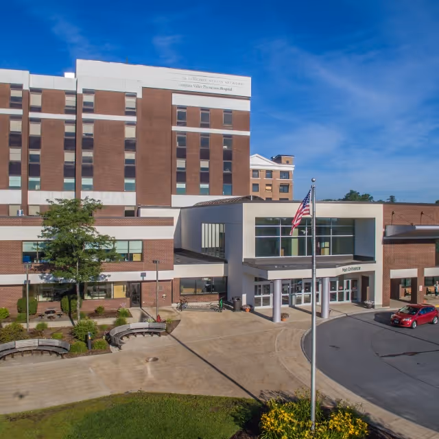 Exterior view of a brick medical facility with main entrance, flagpole, and plaza.