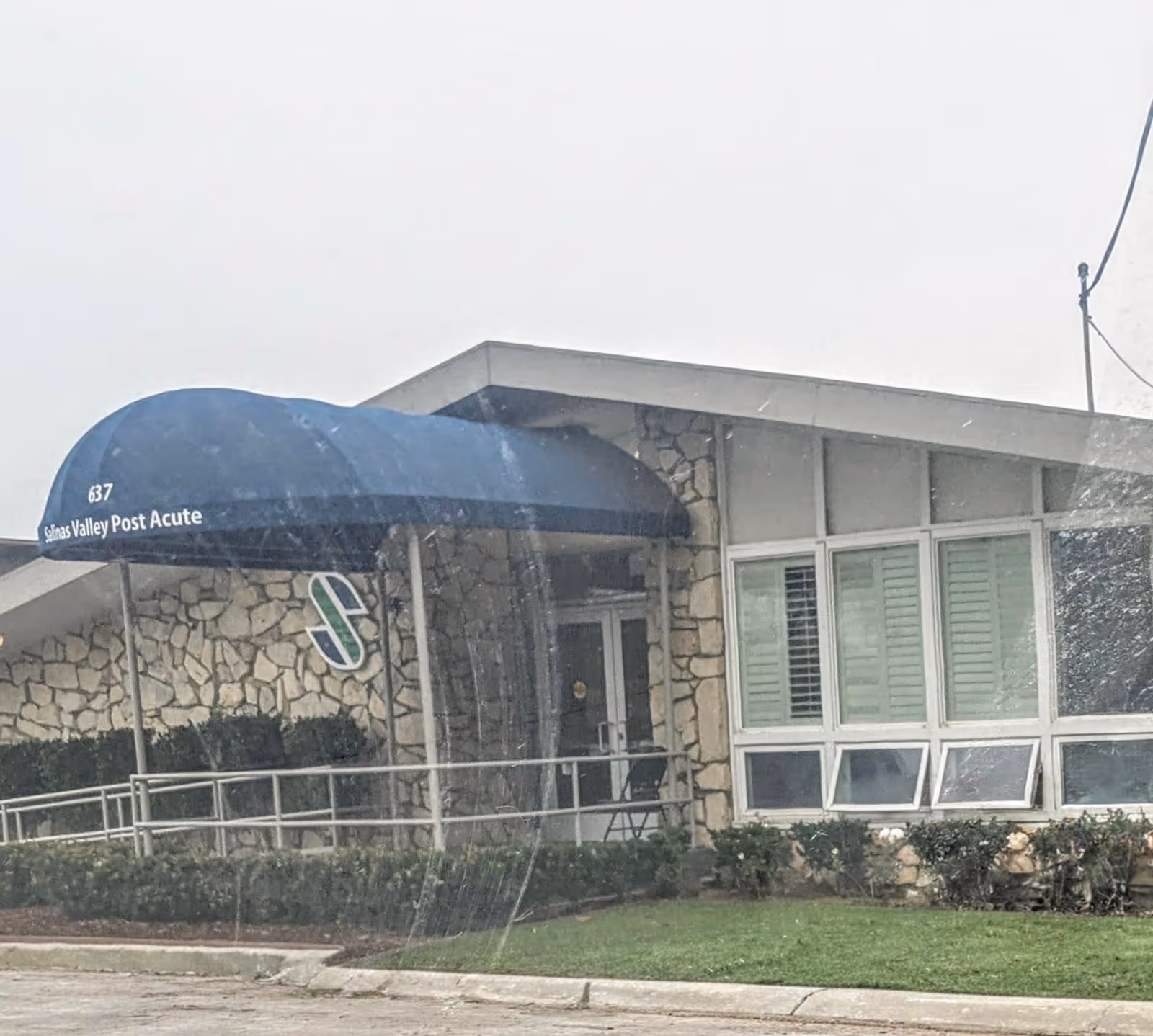 Exterior view of Windsor Gardens Rehabilitation Center entrance with stone facade and blue awning.