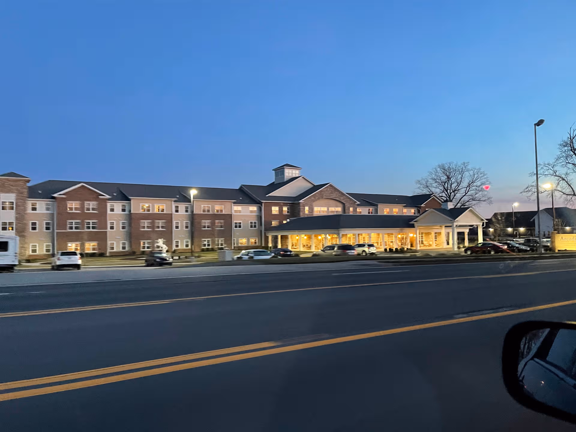 Exterior view of Arcadia Senior Living Bowling Green building along a busy street at dusk.