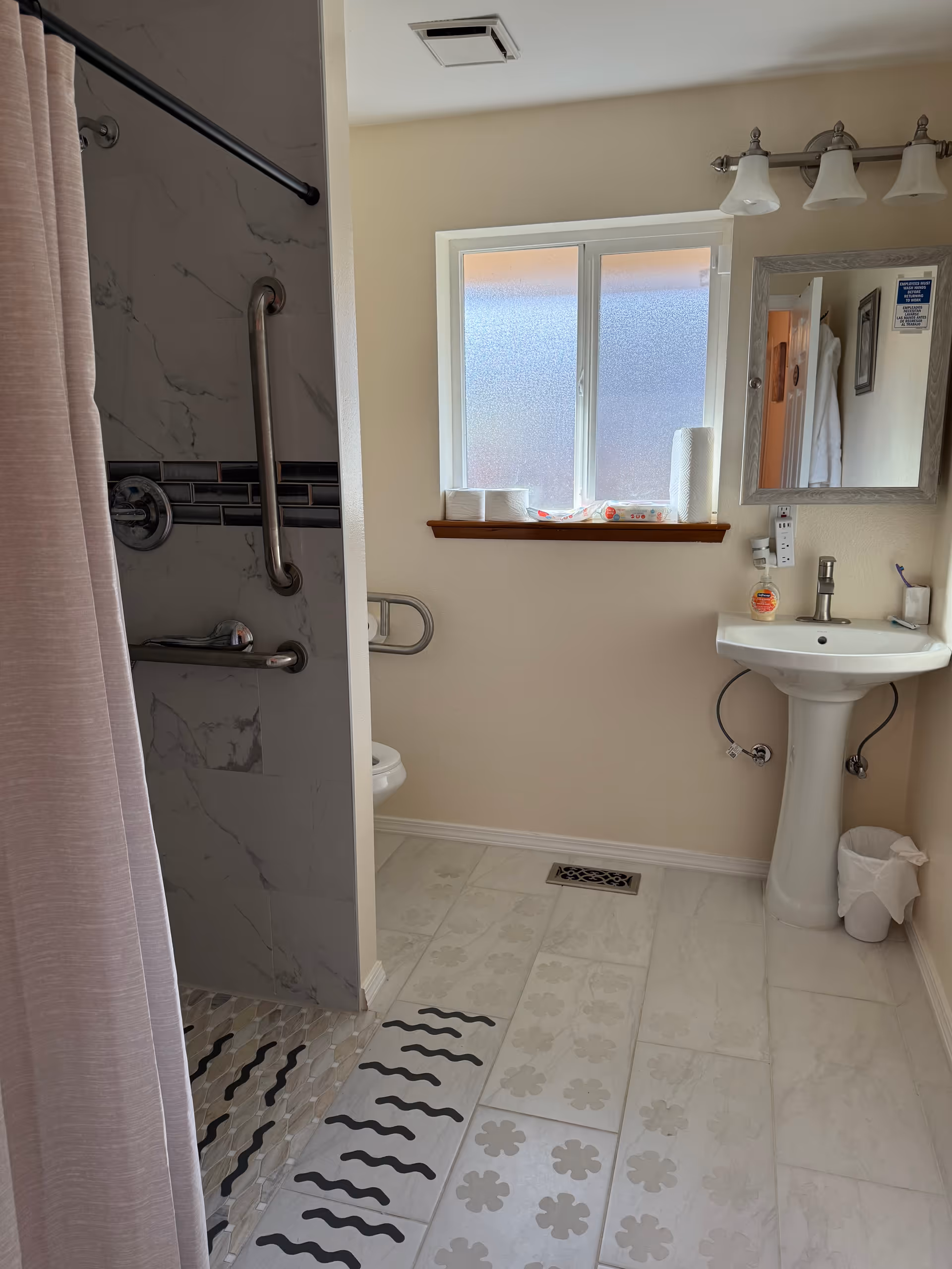 Bathroom with pedestal sink, window, shower with pink curtain, and grab bars.