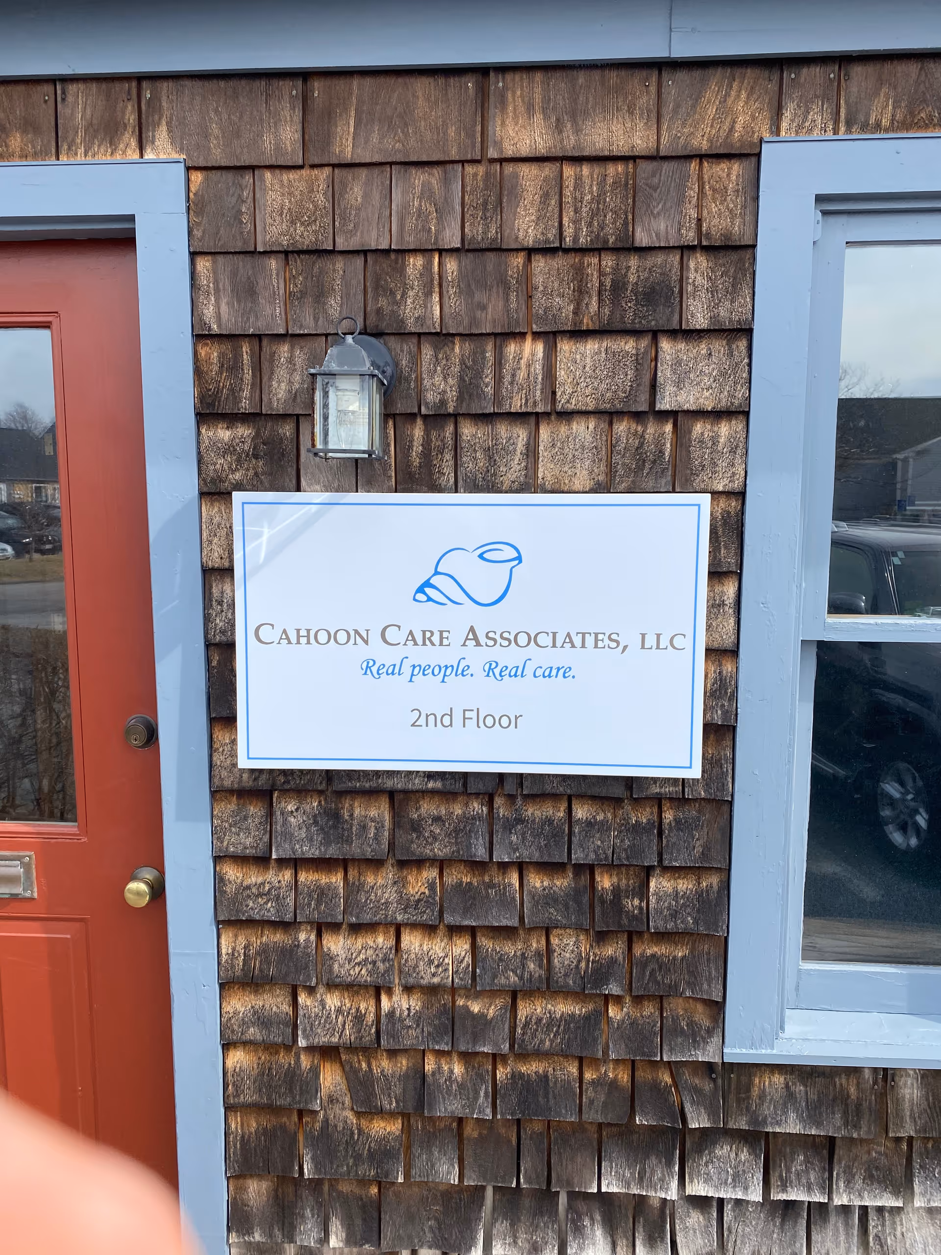 Wood-shingled exterior with a Cahoon Care Associates LLC sign beside a red door.