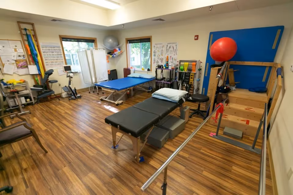 Therapy room with treatment table, exercise equipment, parallel bars, and wooden floor.