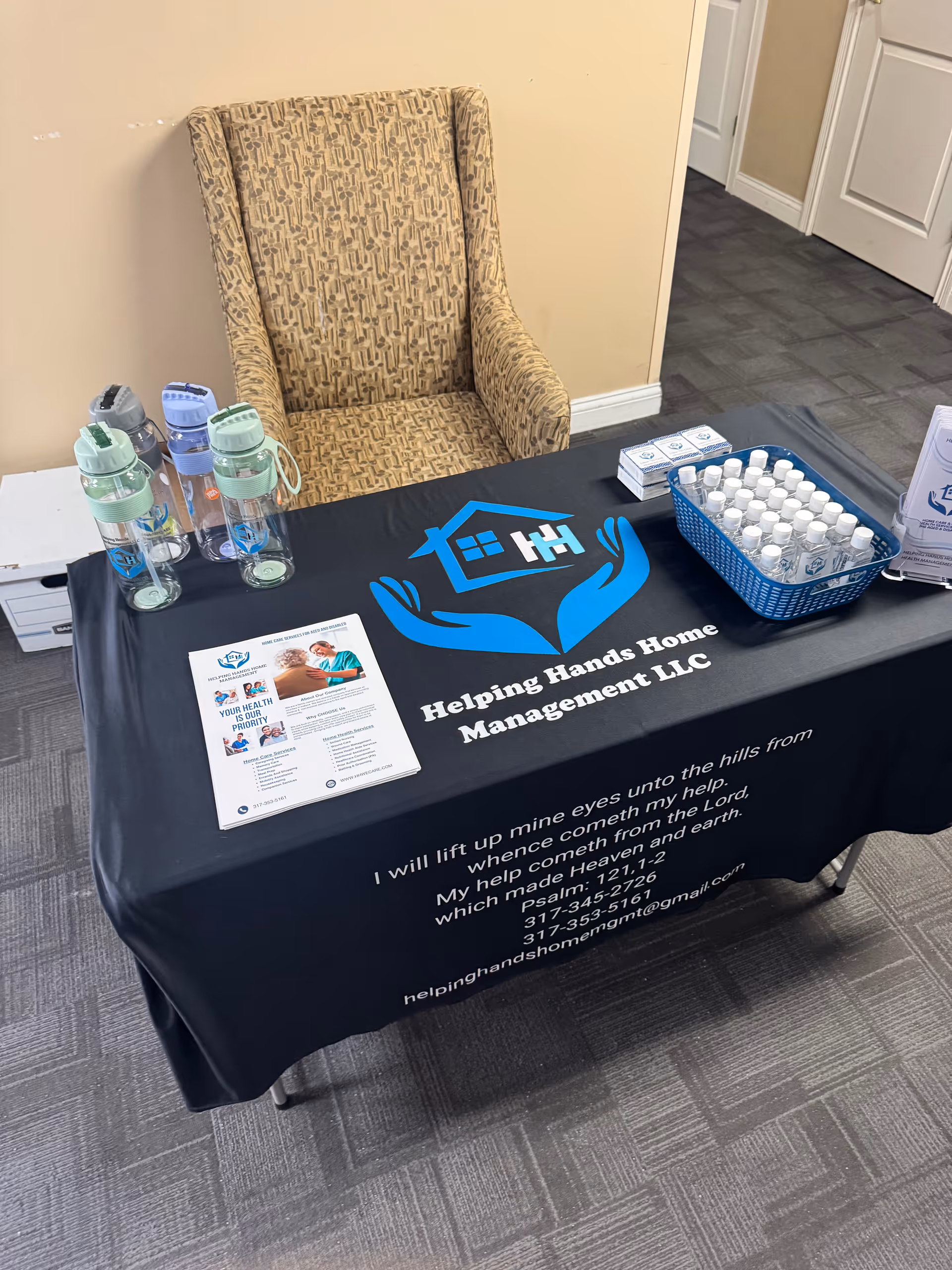 Reception table with Helping Hands logo, water bottles, and brochures in an interior hallway.