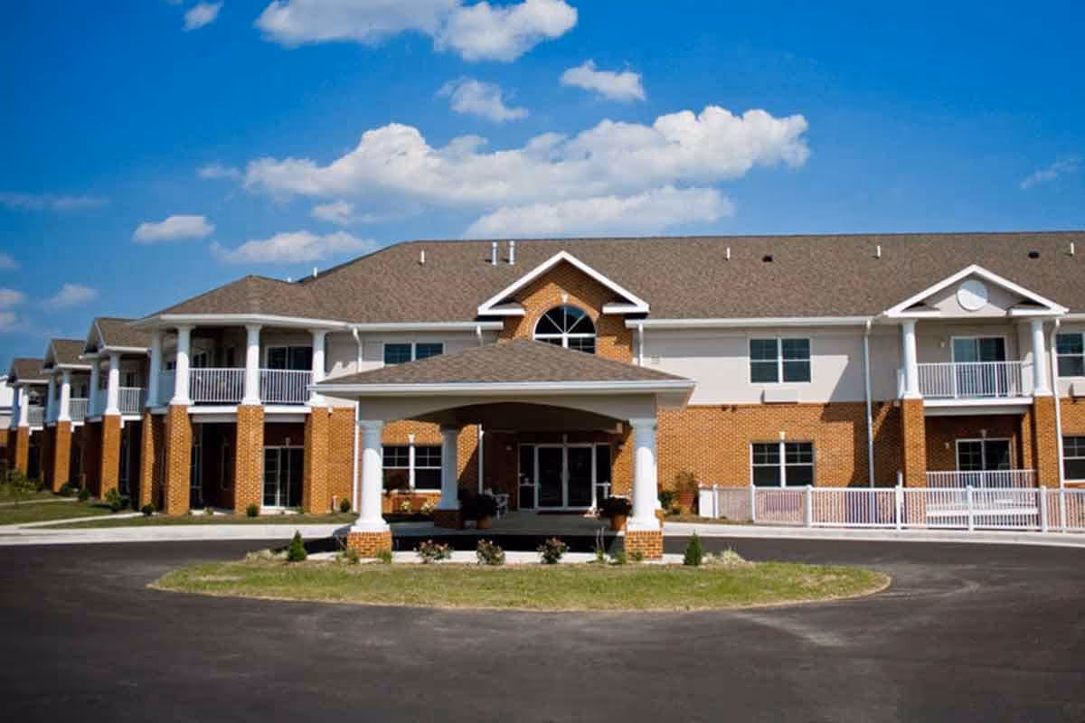 Front exterior of a two-story brick and siding senior living building with a covered porte-cochere and balconies.