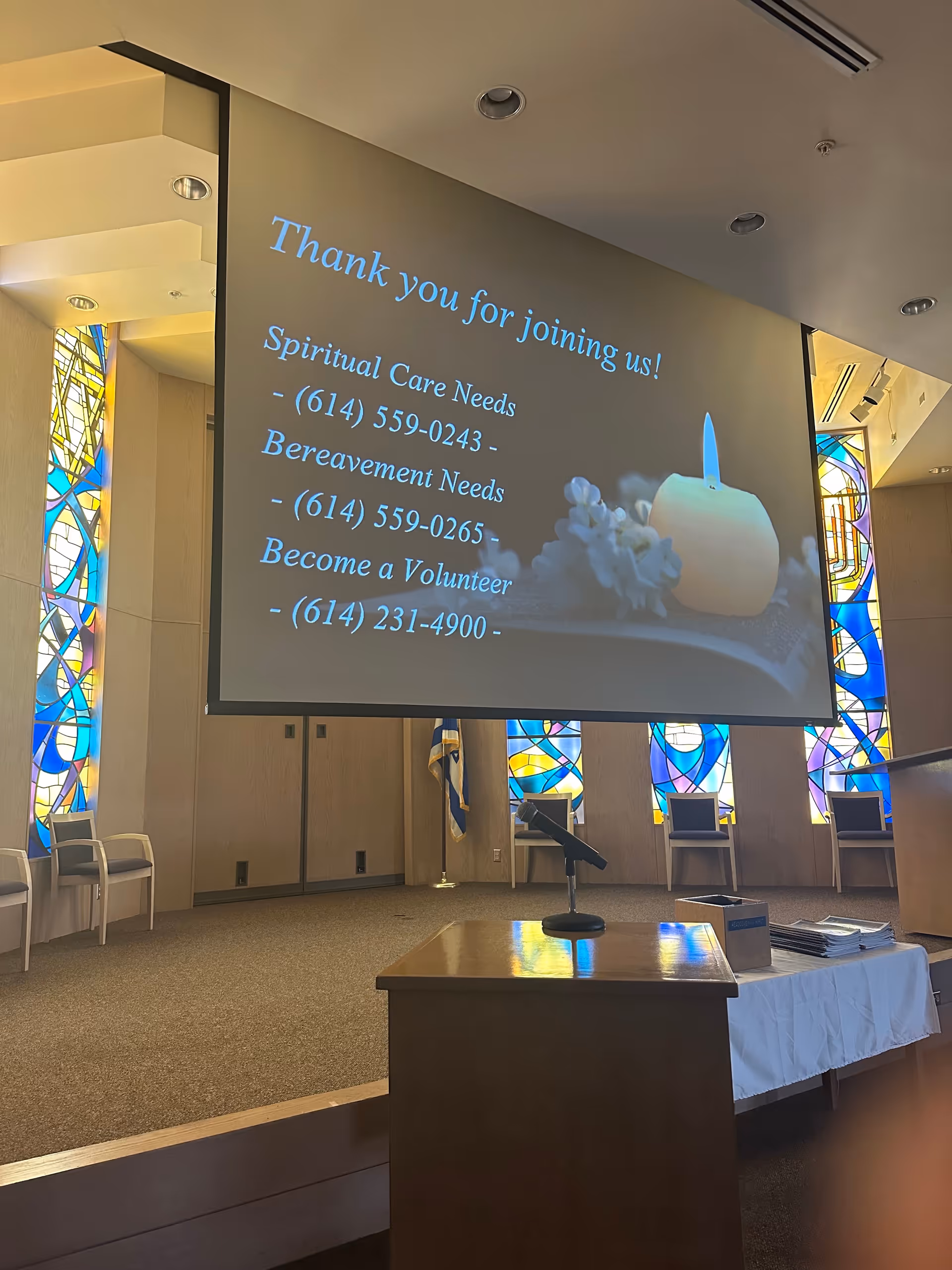 Indoor auditorium at a senior living facility with a large projection screen and stained glass.