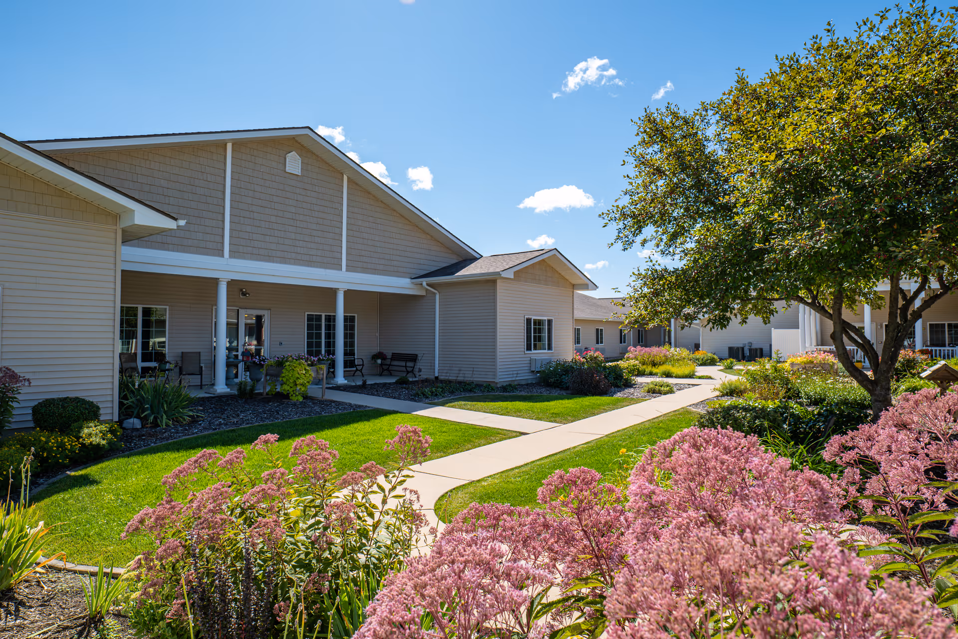 Exterior view of Landings of Kaukauna with a walkway, porch seating, and flowering landscaping.