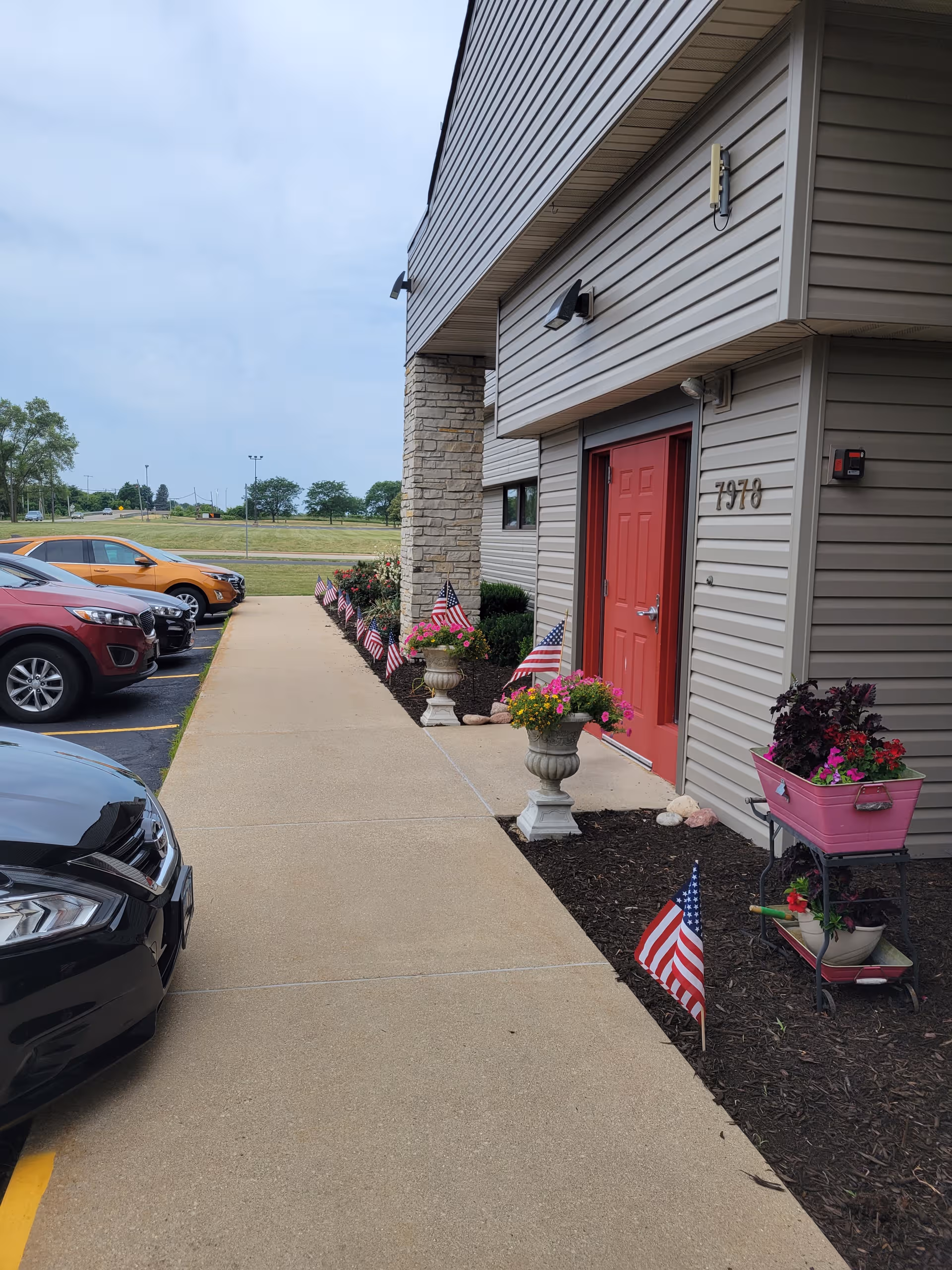Exterior view of Anam Care, Inc. facility entrance with red door, cars, and patriotic decorations.