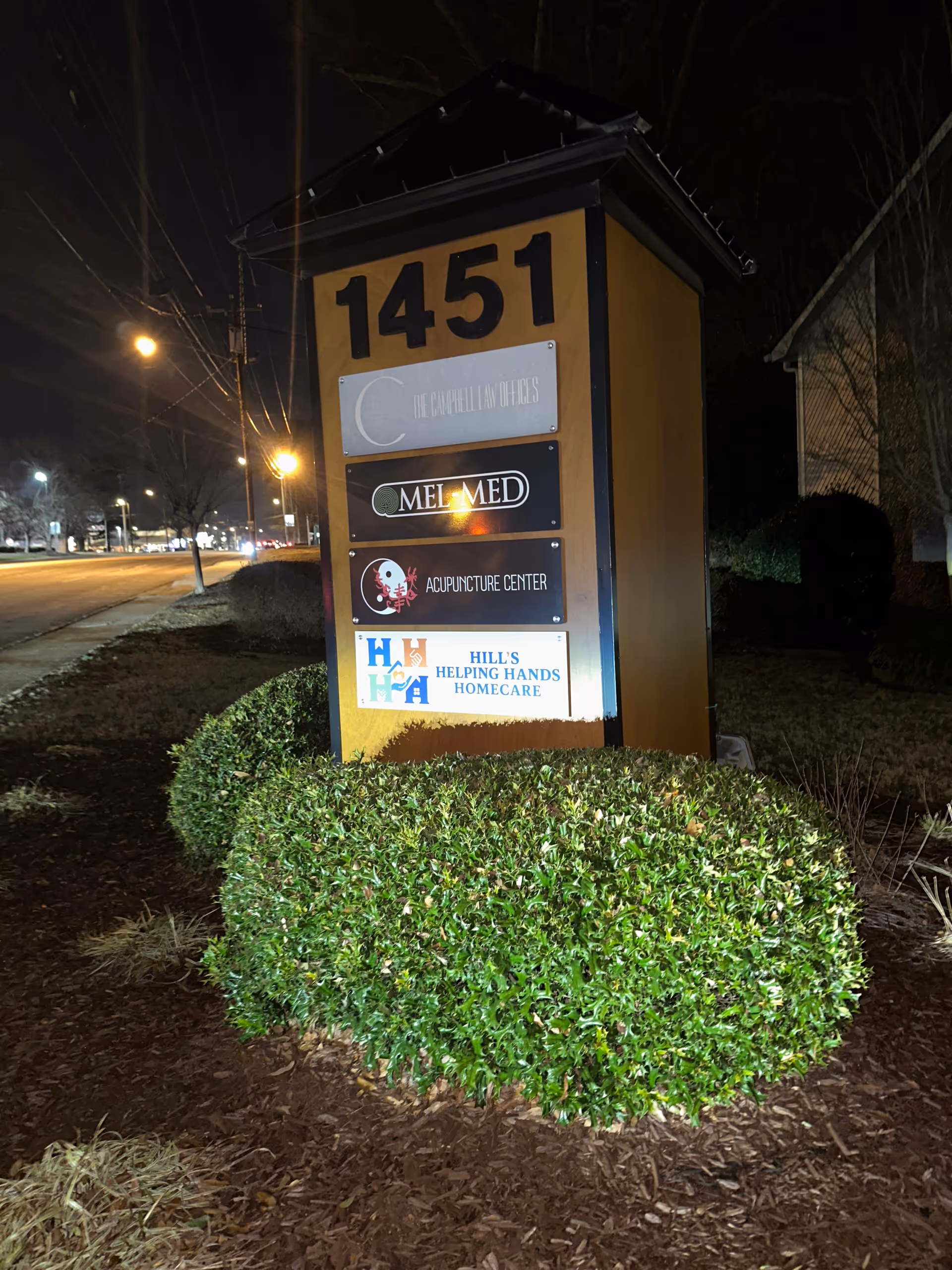 Tall sign with address 1451 and multiple business plaques in a landscaped front yard at night.