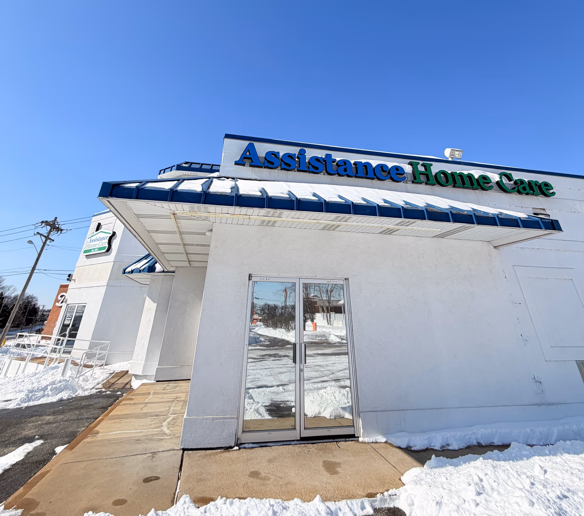 White building with Assistance Home Care sign and glass doors under a blue awning.