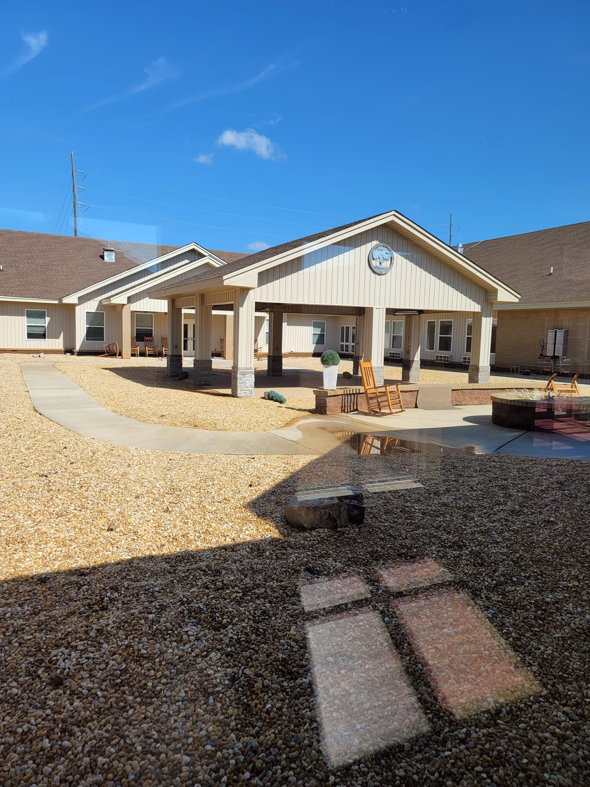Sunlit exterior of a Lodge senior living facility with a covered entrance and seating area.
