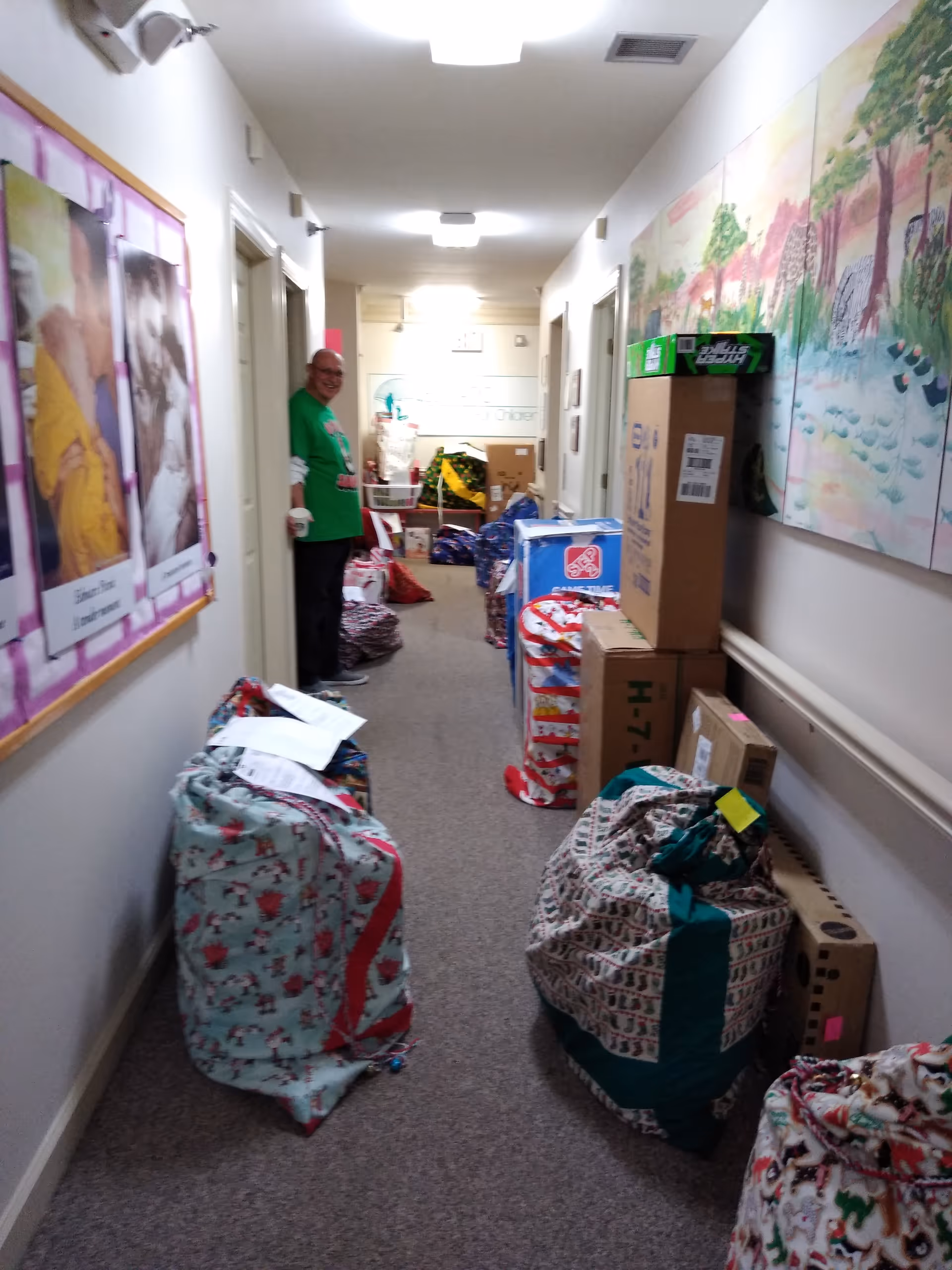Long hallway in a senior living facility filled with gift bags, boxes, and a man standing.