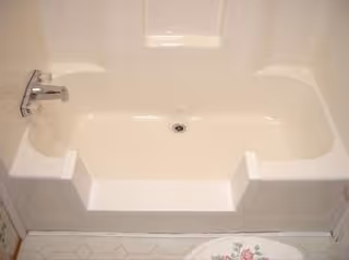 White bathtub with built-in steps and faucet in a tiled bathroom.