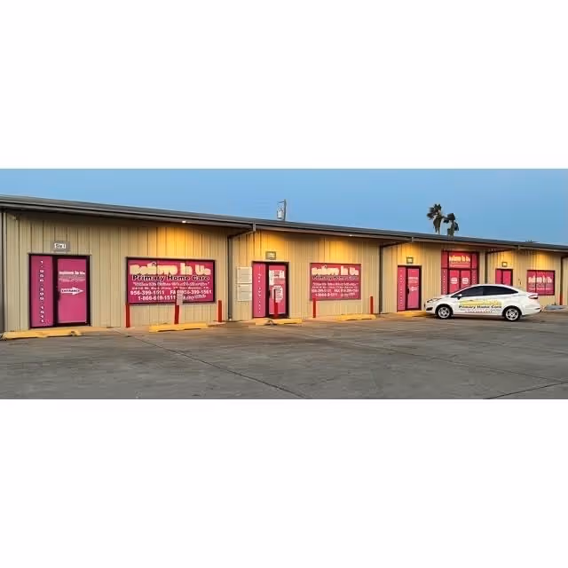 Long beige commercial building with pink doors and signs, a white car parked outside.