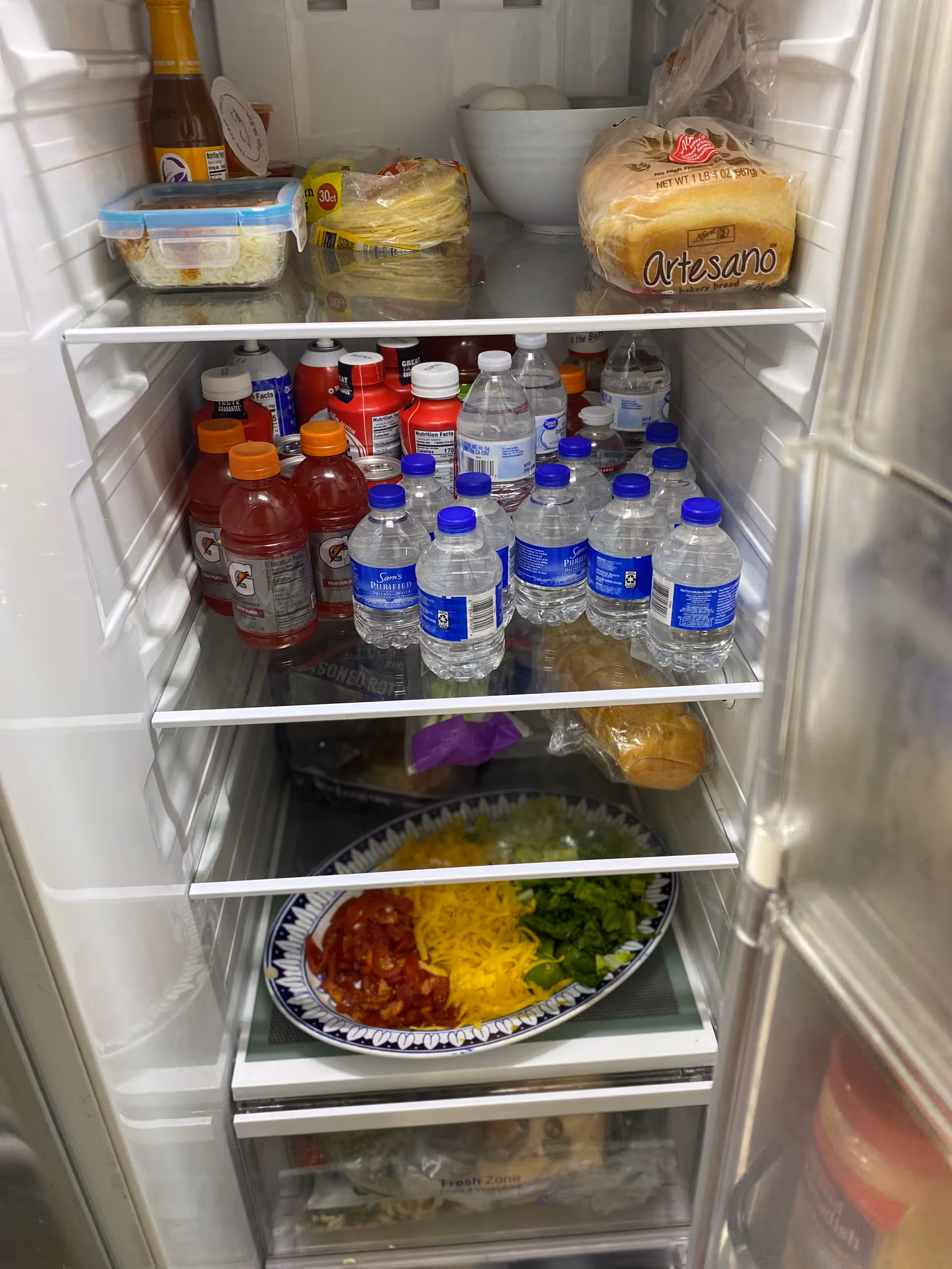 Open refrigerator stocked with water bottles, beverages, bread, eggs, and a plated meal.