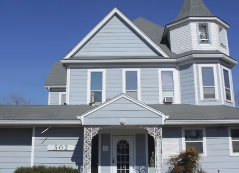 Blue Victorian-style building with peaked roof, front porch, and turret.