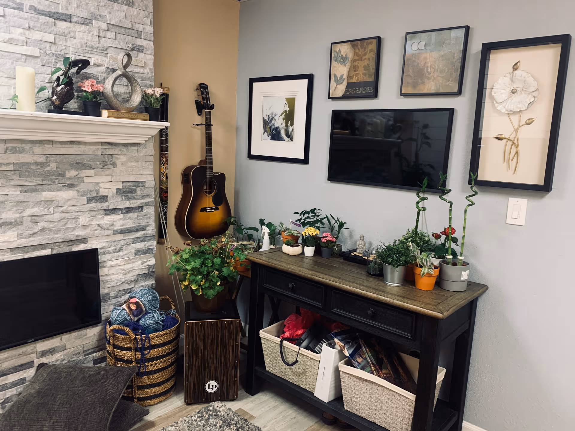Cozy living room corner with fireplace, guitar, plants, framed art, and a TV.