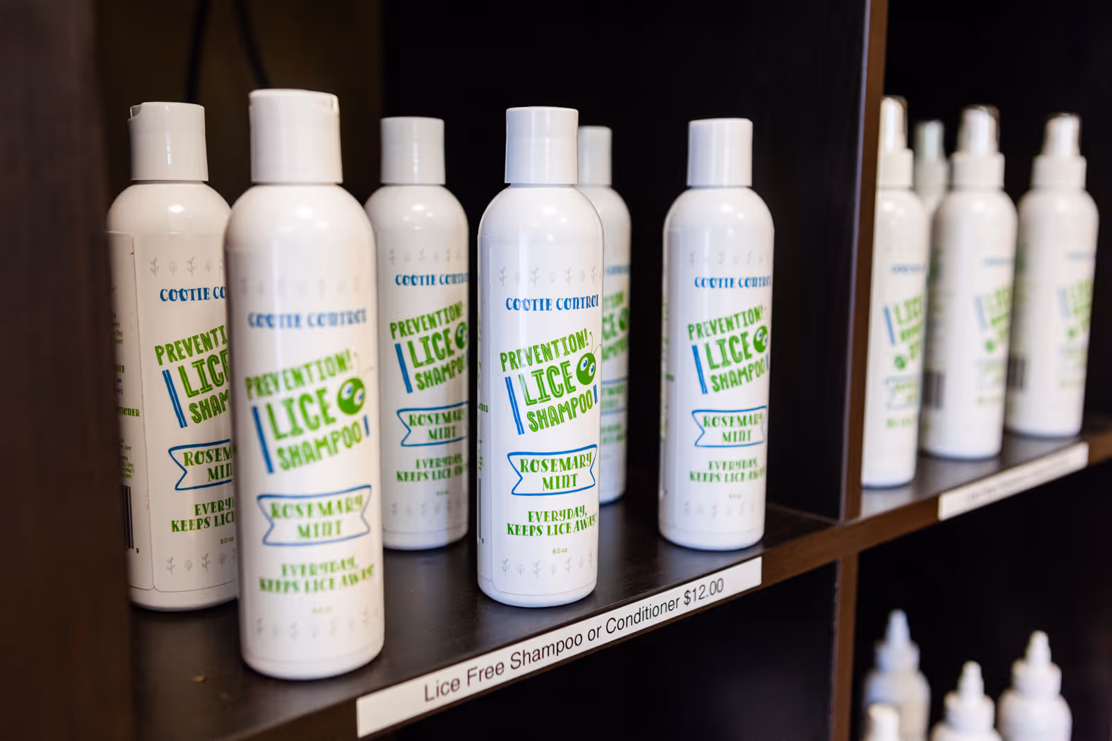Shelf of white lice shampoo bottles on dark wooden shelving inside facility.