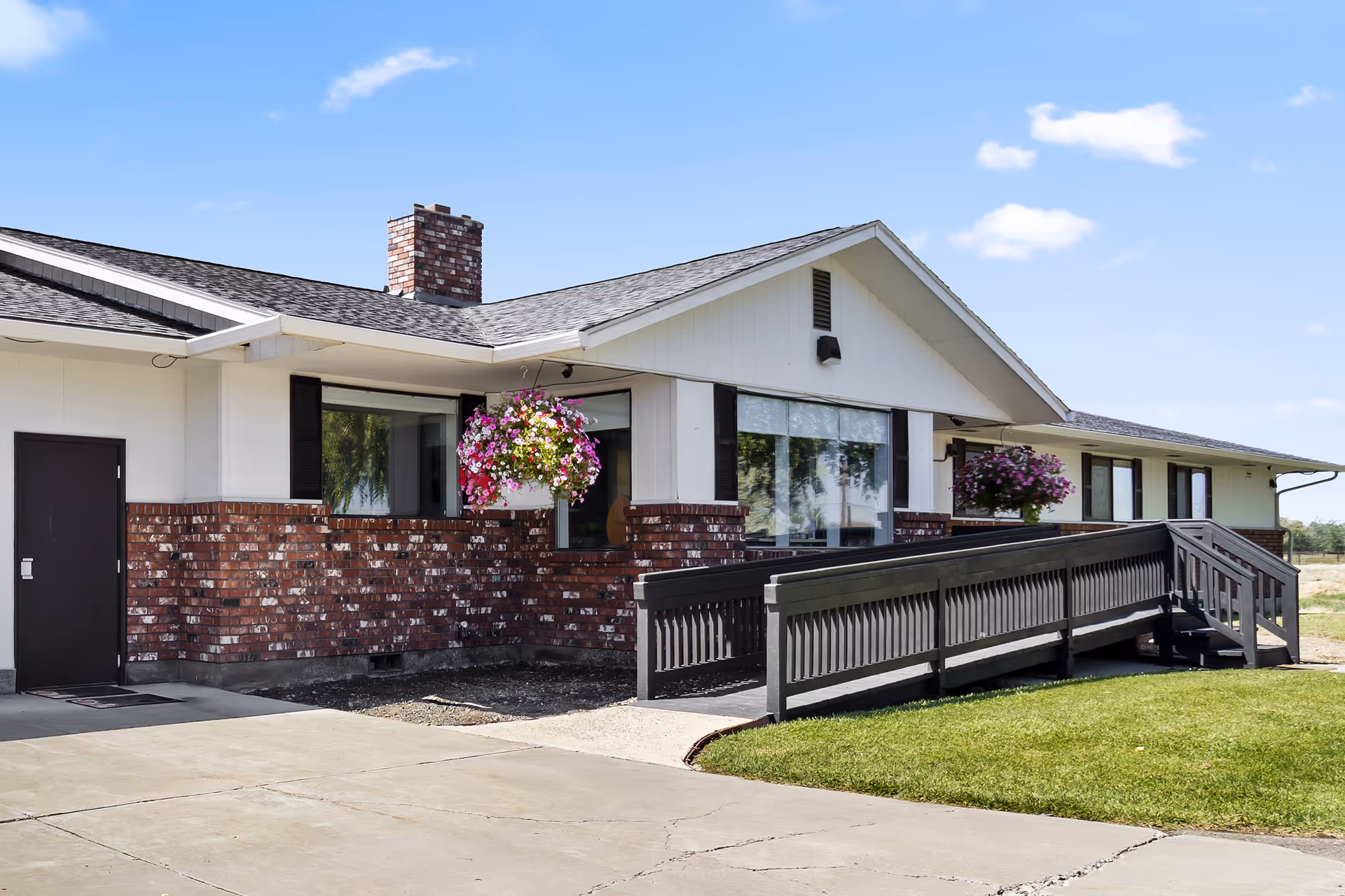 Single-story Heartlinks Adult Family Home exterior with brick lower facade, white siding, ramp, and hanging baskets.