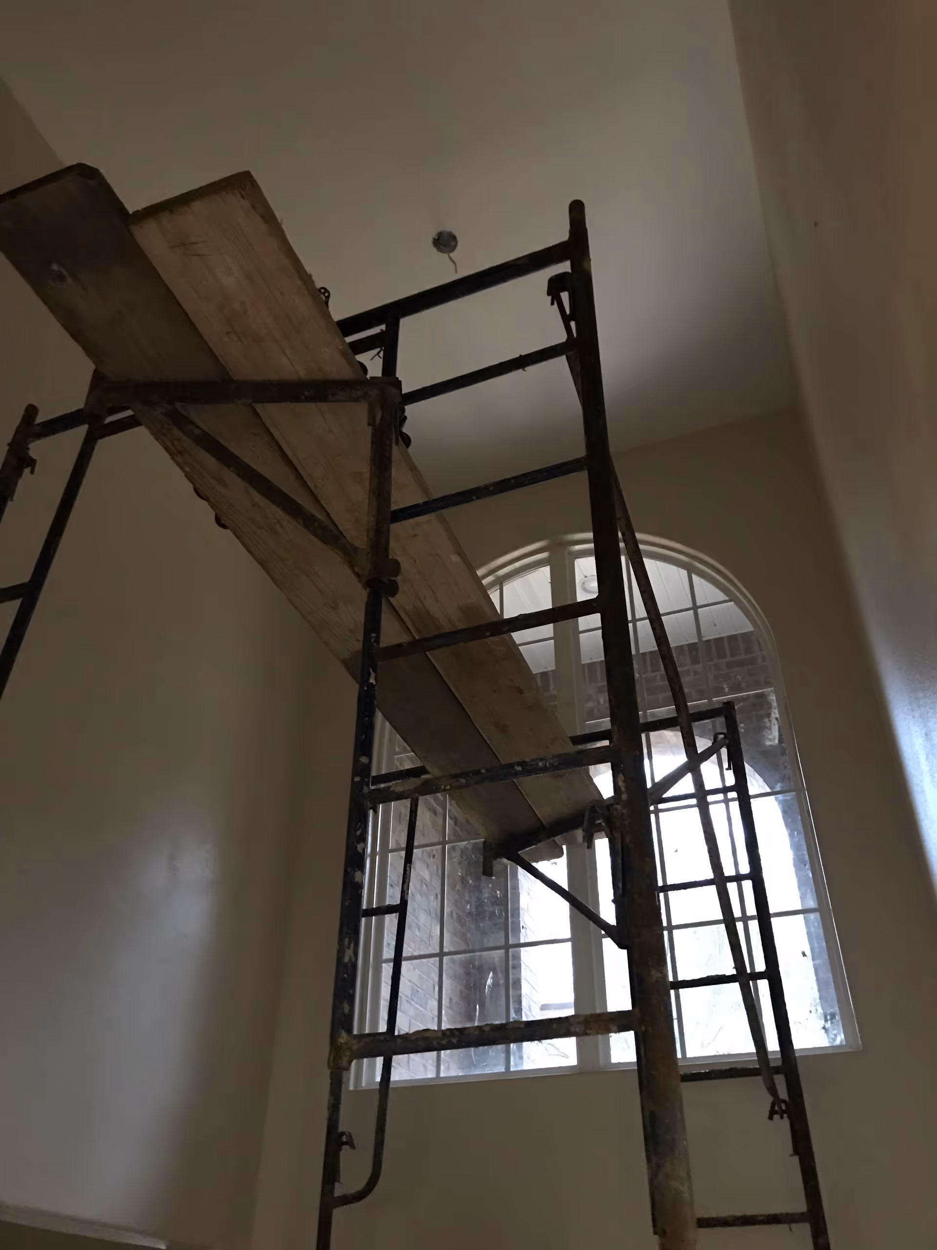 Tall metal scaffold dominates an interior room beside a large arched window.