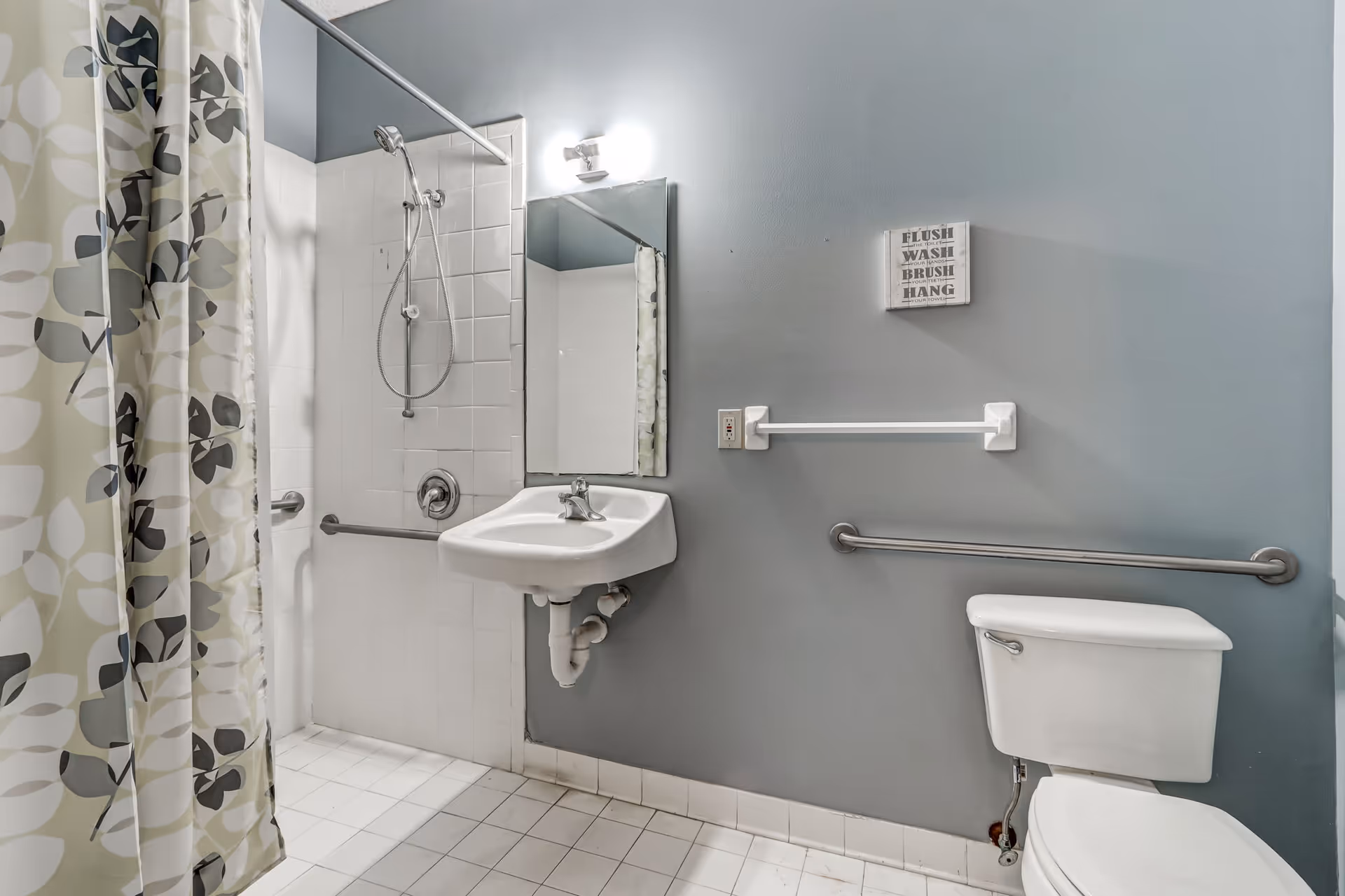 Accessible bathroom with shower, sink, toilet, patterned curtain, and safety rails.