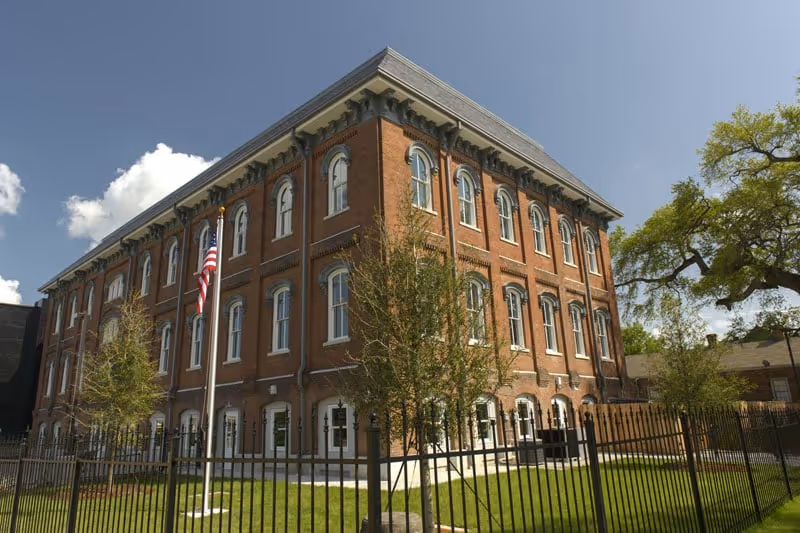 Exterior view of Belleville senior living building, brick facade with flag, trees, and a fence.