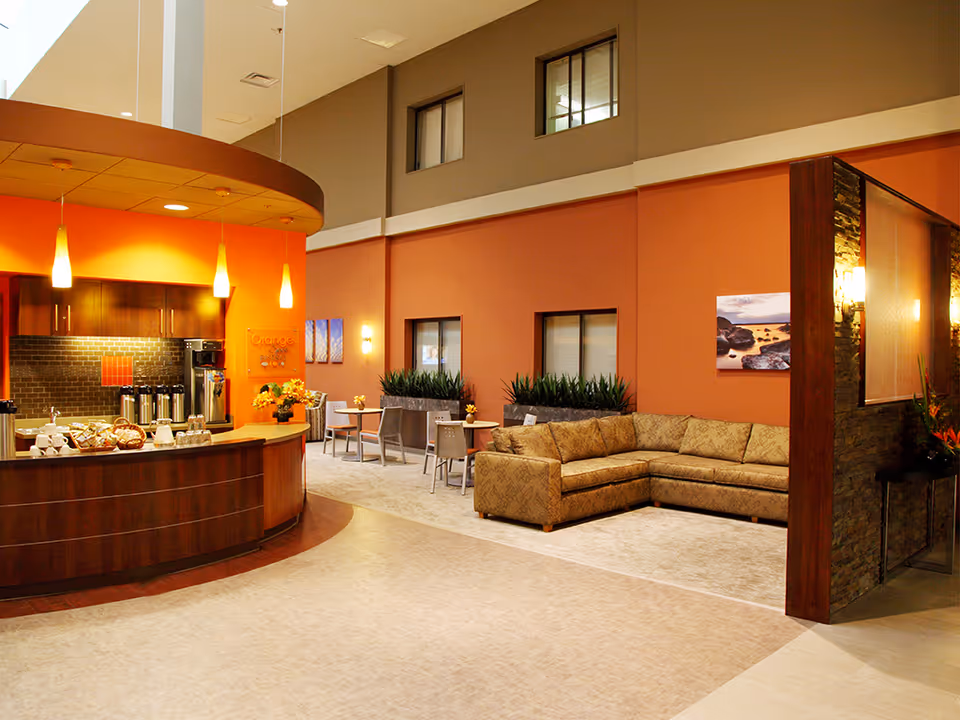 Warm, spacious senior living lobby with curved coffee counter and beige seating.