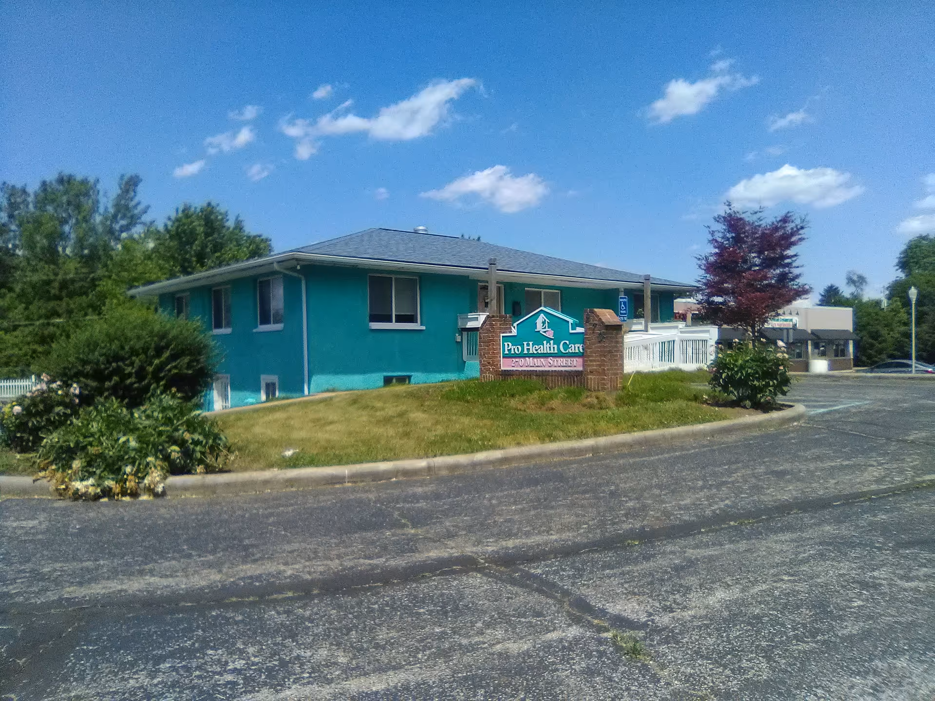 Exterior view of a turquoise senior care facility with a sign in front and parking lot.