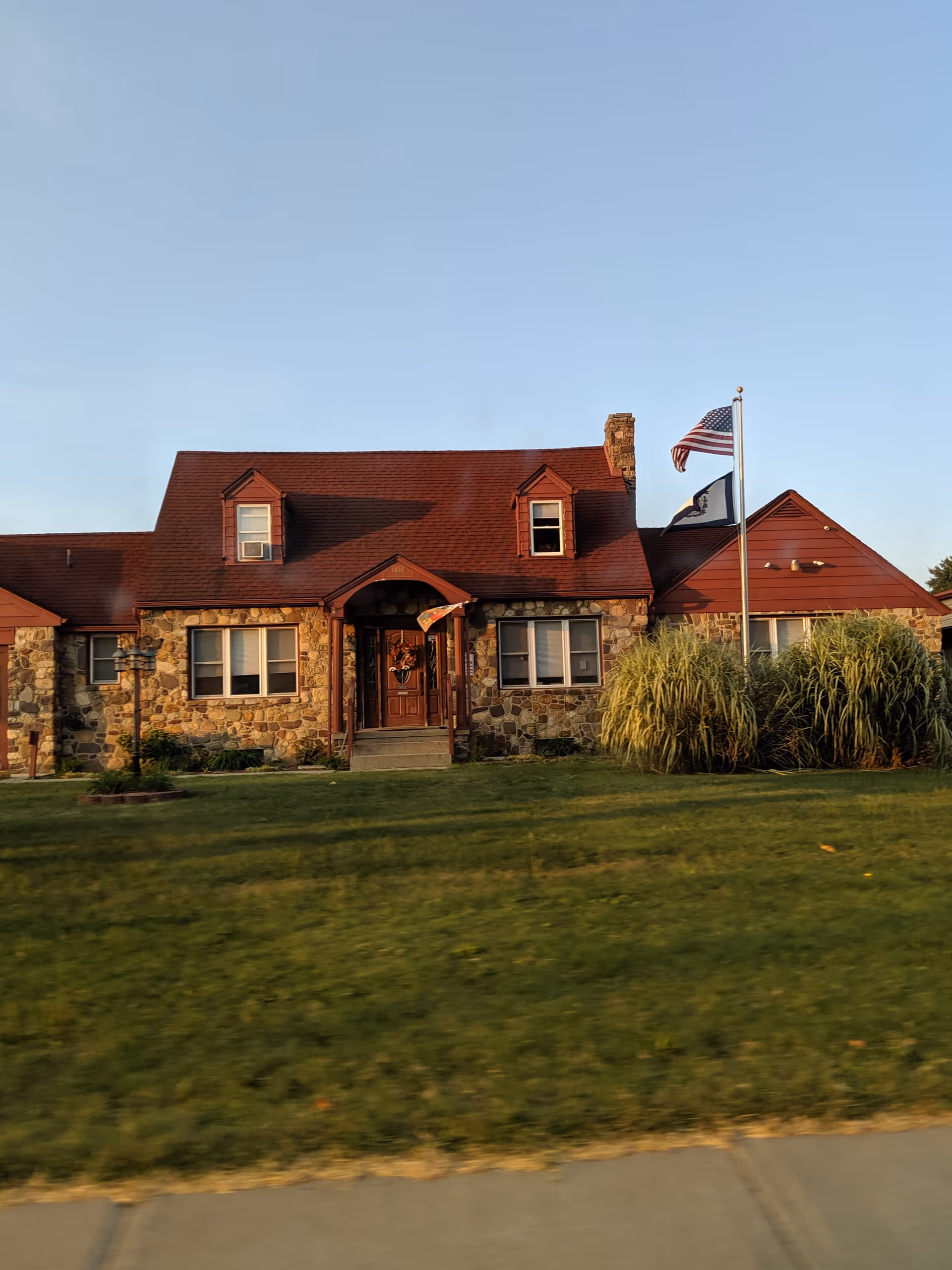 Front view of a stone building with red roof, flags, and manicured lawn.