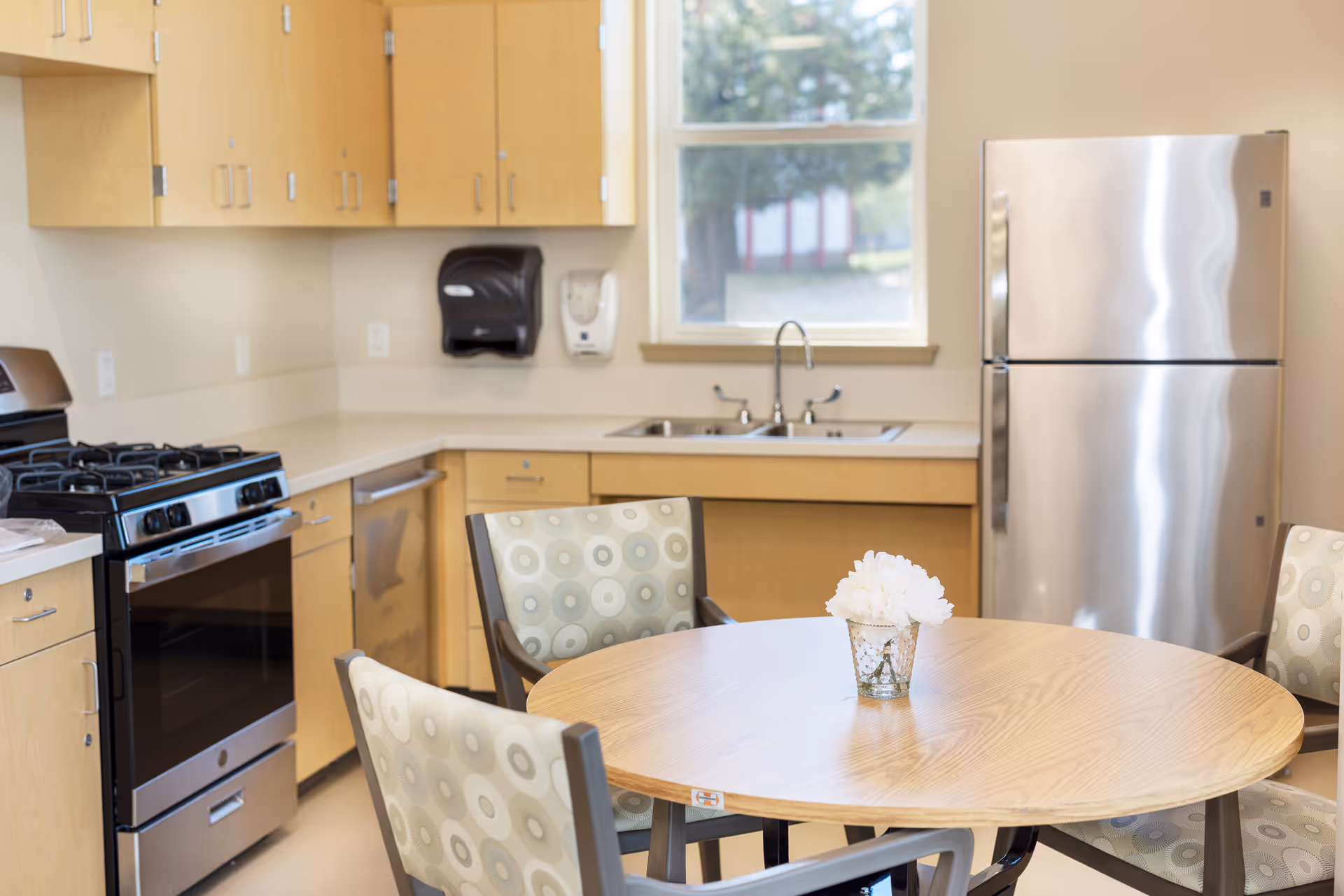 A bright kitchen with wooden cabinets, stainless steel fridge and stove, and a round dining table.