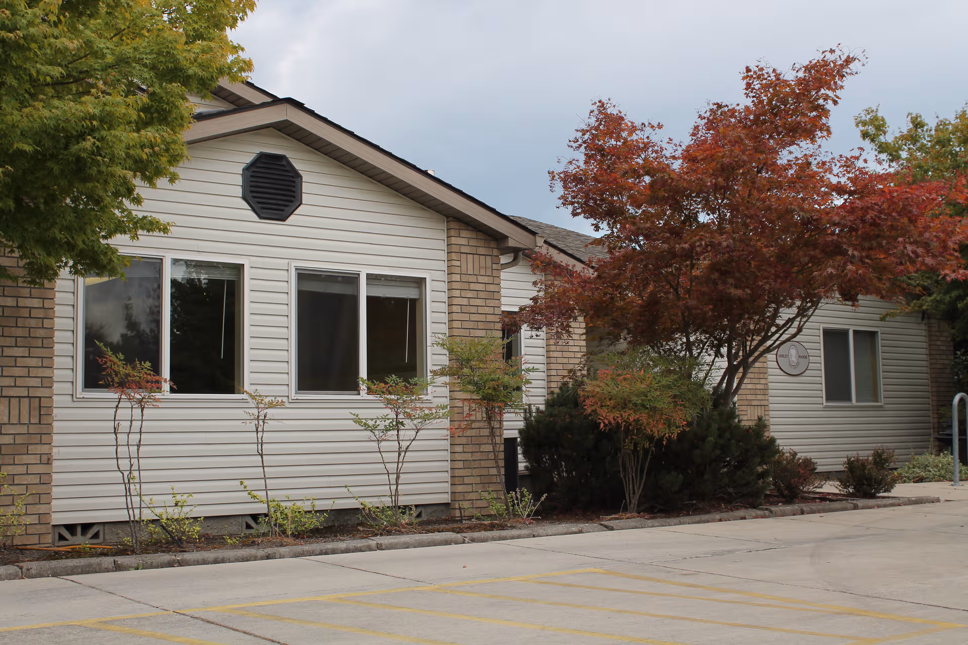 Beige, single story building exterior with large front windows and autumn trees along the front