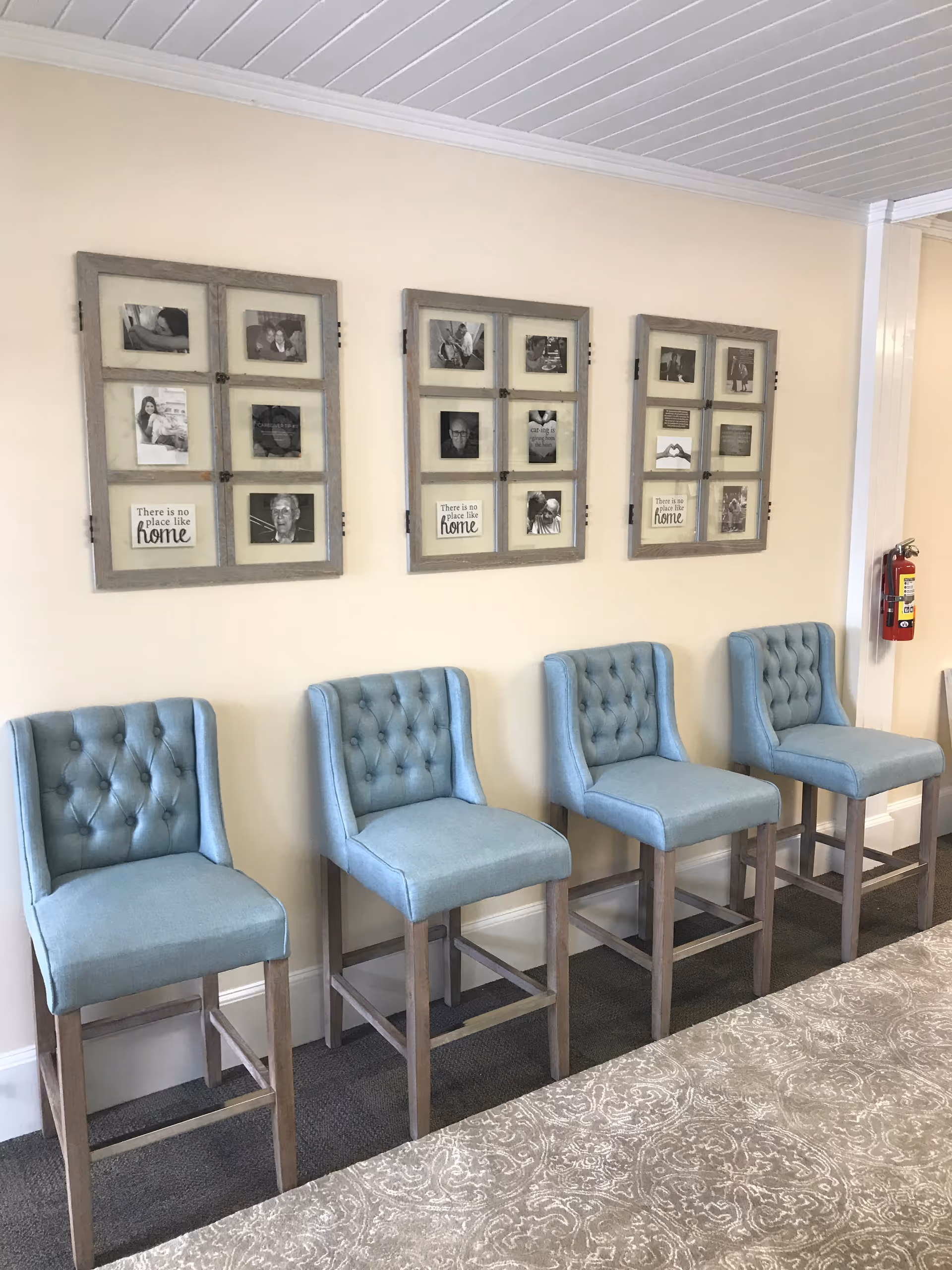 Row of light blue tufted chairs along a wall with photo frames and a fire extinguisher.