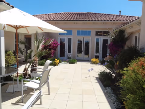 Outdoor patio area with seating, umbrellas, and flowering plants at Villa Ambrosia