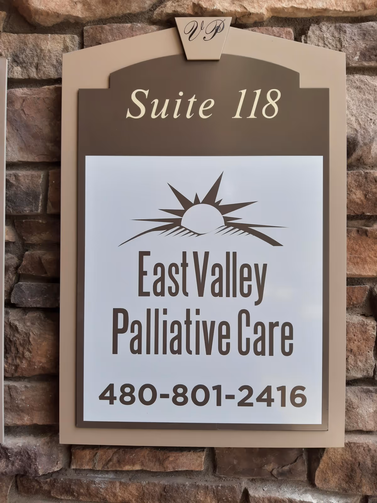 Beige sign on a stone wall reading East Valley Palliative Care, Suite 118.