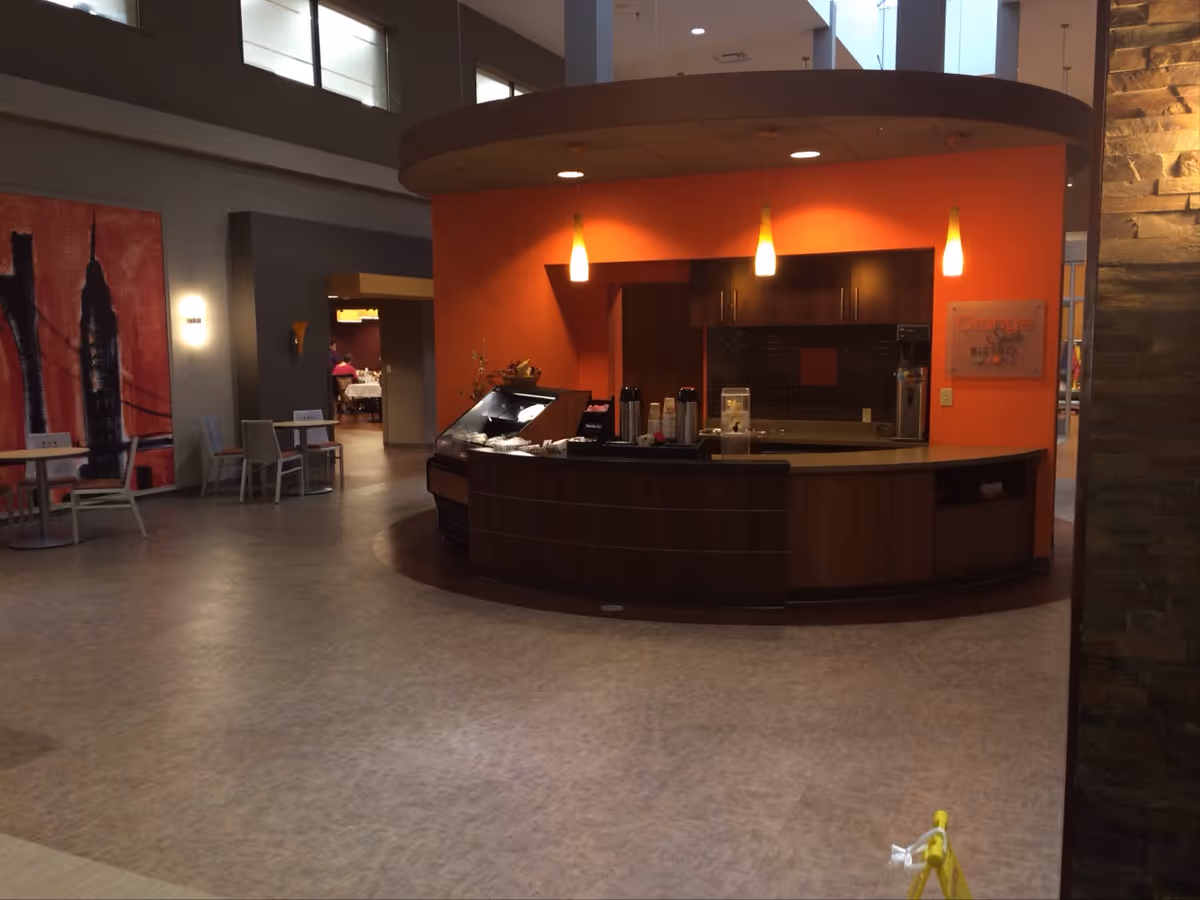 Curved wooden front desk with orange wall, warm lighting, and seating area in a modern lounge.