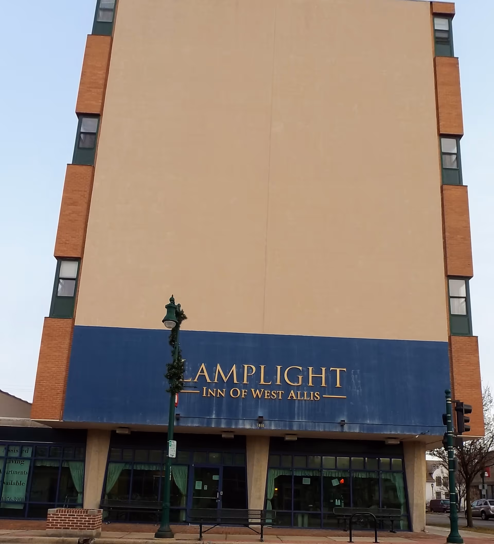 Tall beige building with blue sign reading Lamplight Inn of West Allis at the entrance.