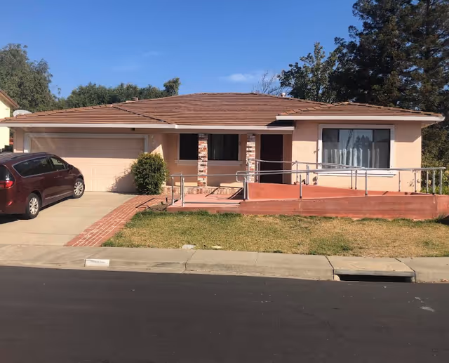 Single-story peach house with ramp entrance and a parked car in driveway.
