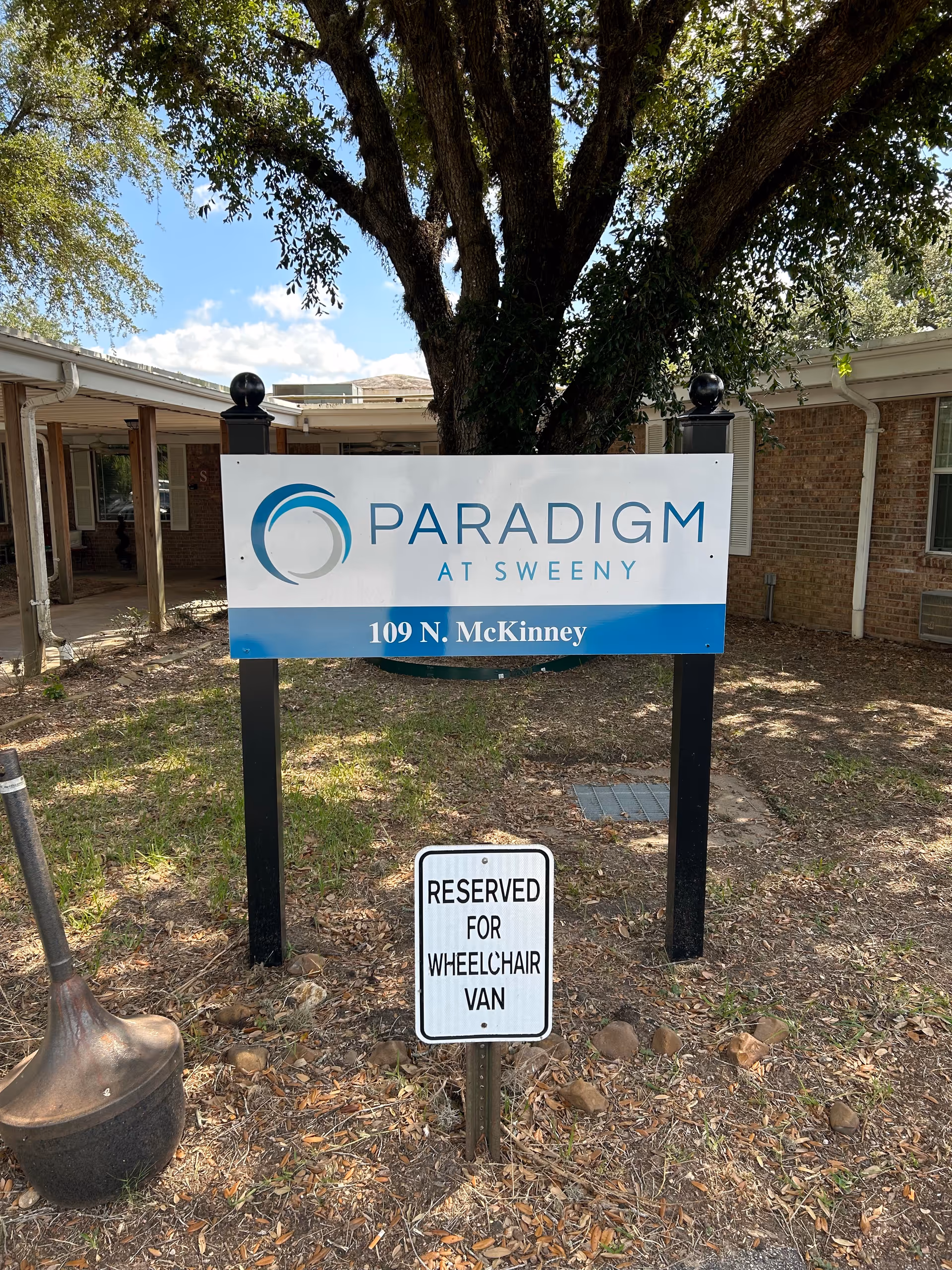 Outdoor view of Paradigm at Sweeney sign in front of brick building with tree.