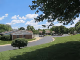 Exterior view of Good Samaritan Village campus with brick buildings, trees, and a curved road.