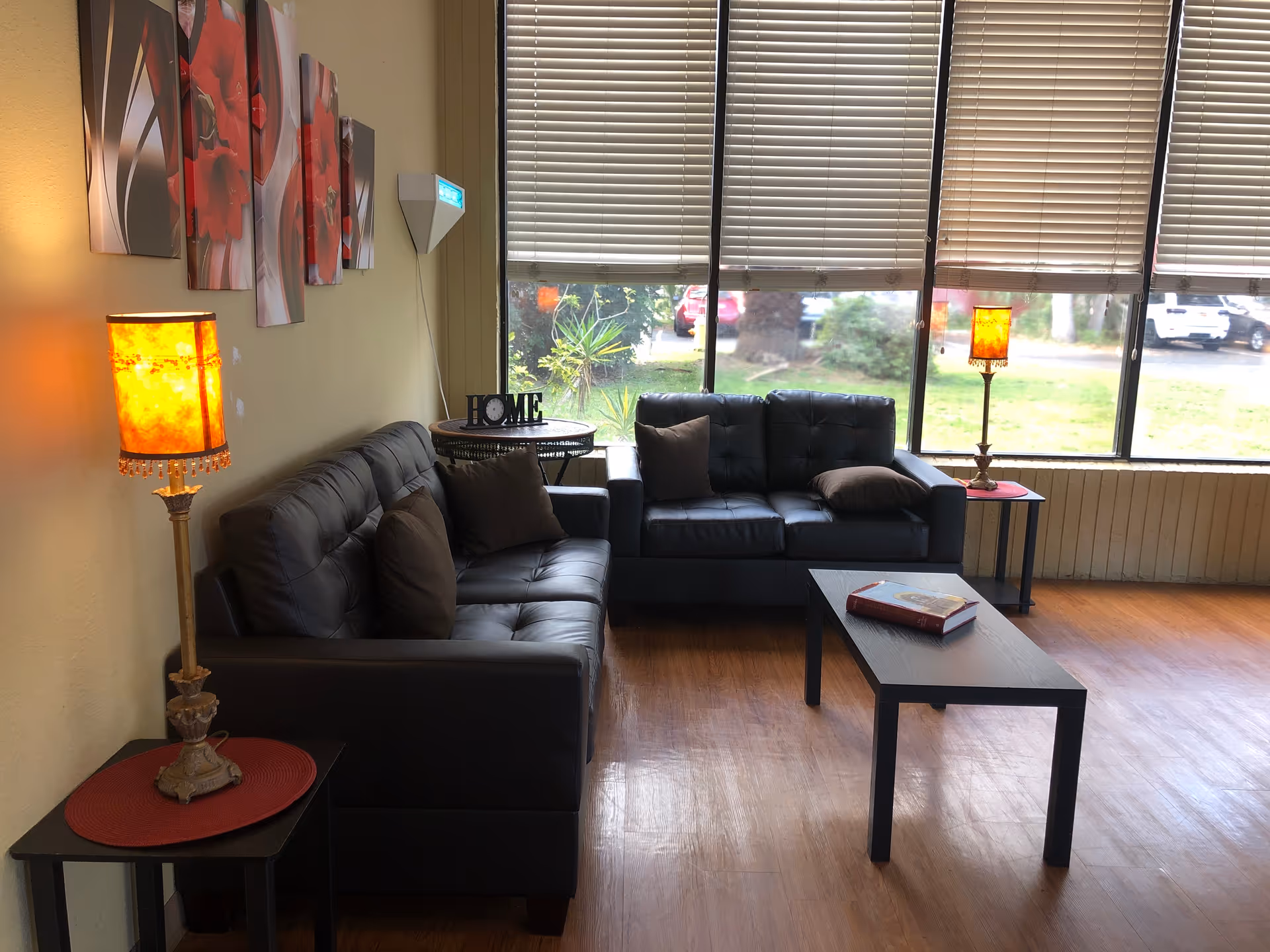 Living room with black leather sofas, coffee table, lamps, and large window blinds.