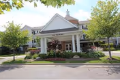 Front entrance of Village of Redford senior living, with white columns and landscaped grounds.