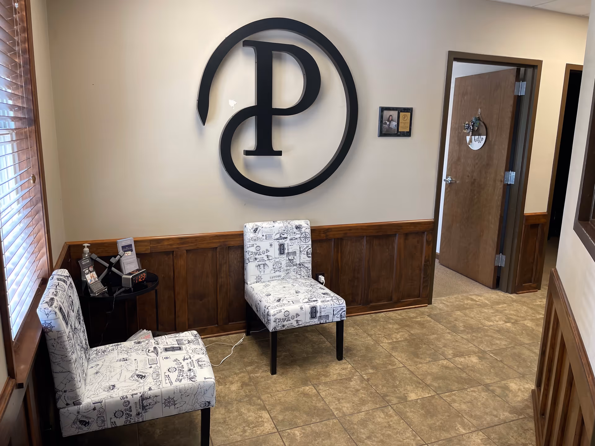 Lobby waiting area with two patterned chairs and a large circular logo on the wall.