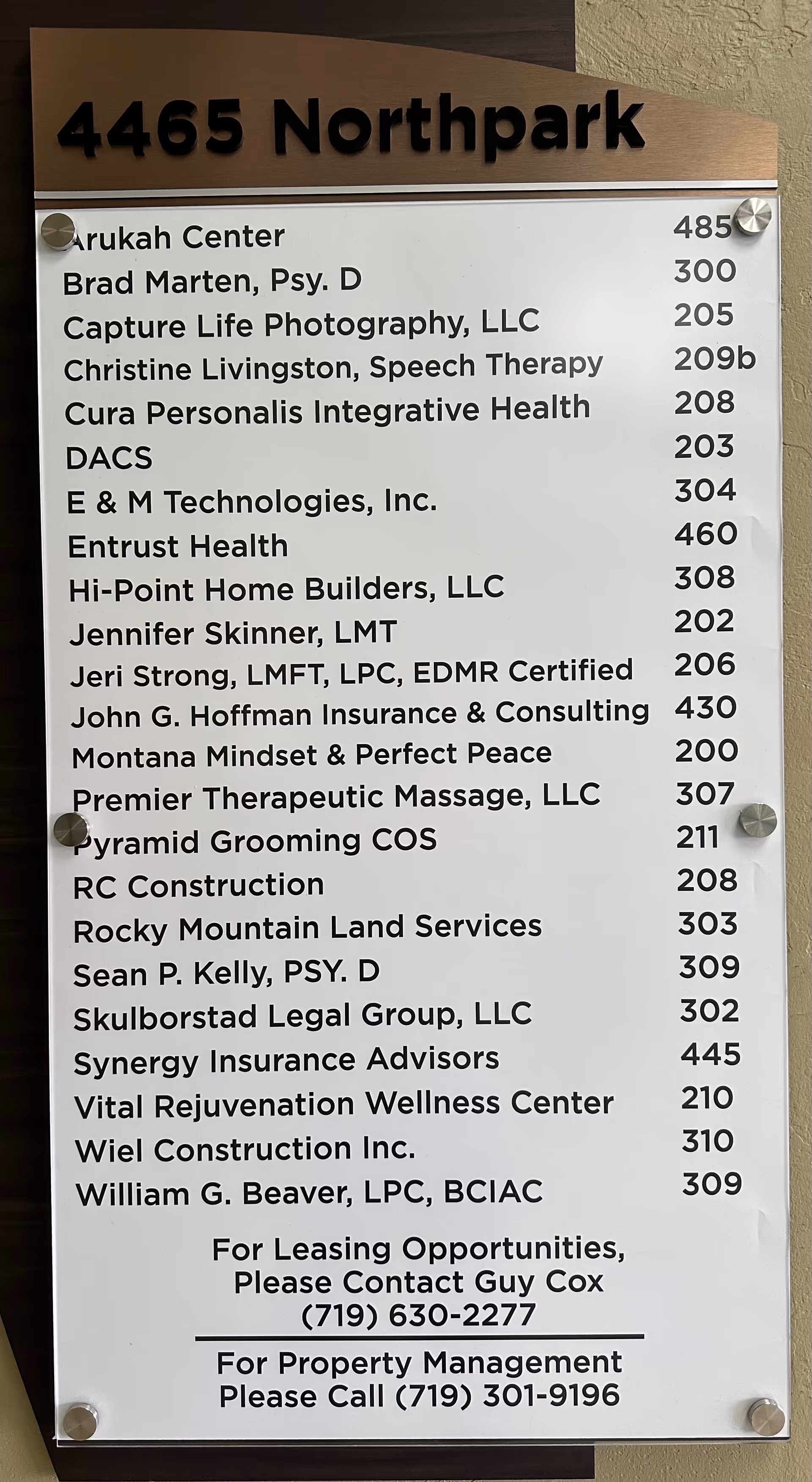 A directory sign with numerous tenant names and unit numbers mounted on a wall.