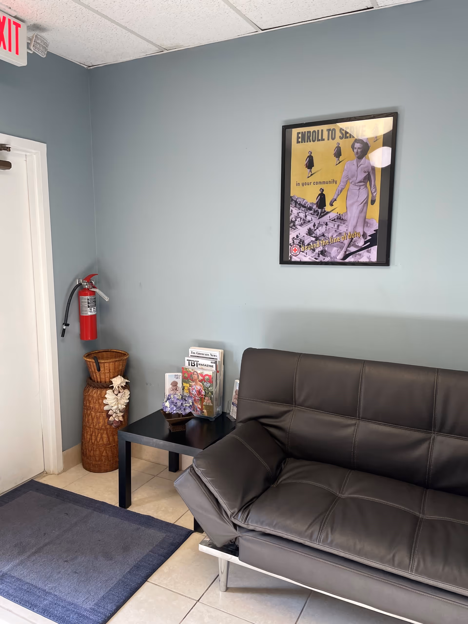 Lobby corner with a black leather sofa, magazines, wall poster, and a fire extinguisher.