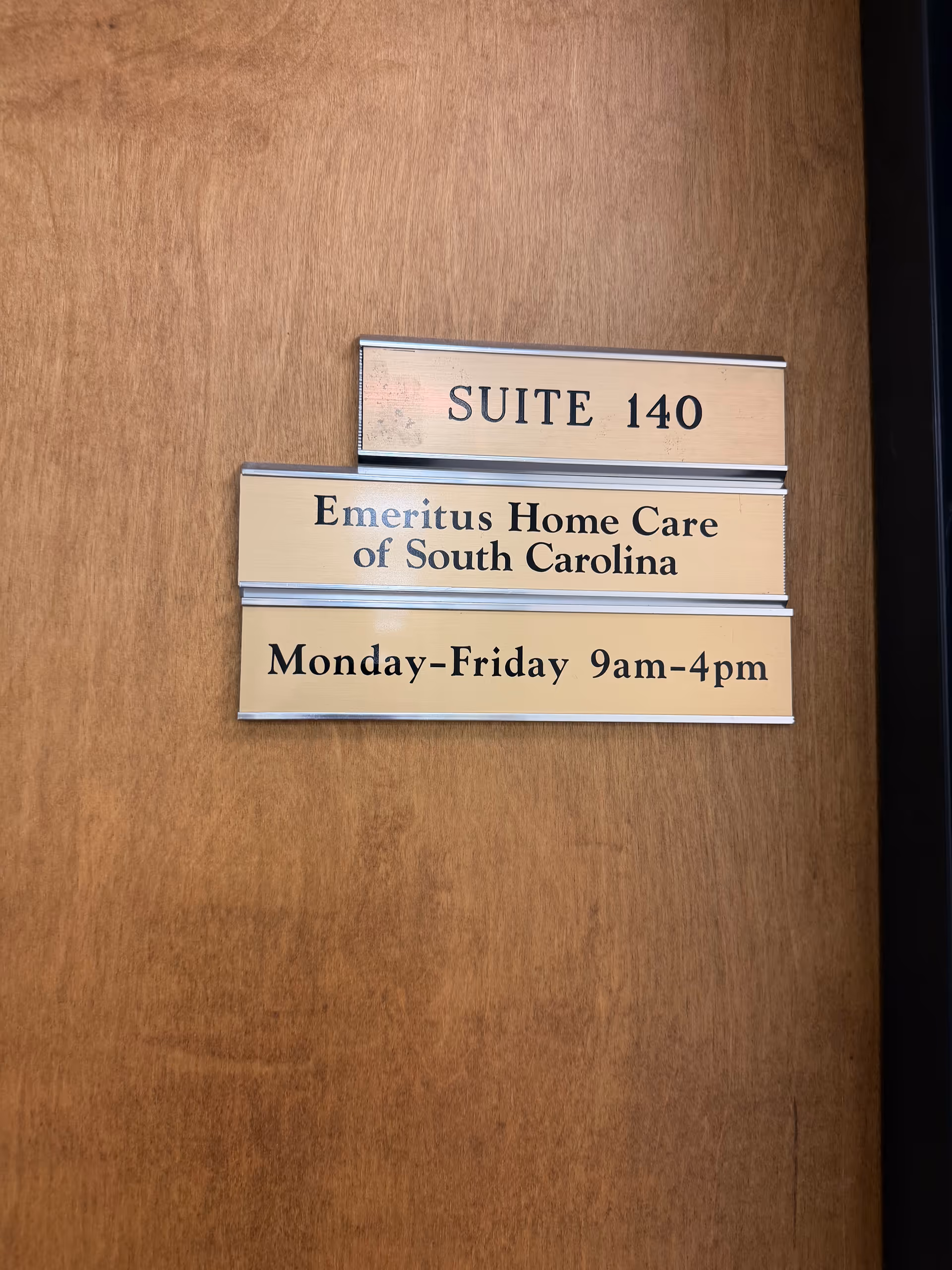Wooden door with three plaques displaying Suite 140 and Emeritus Home Care hours.
