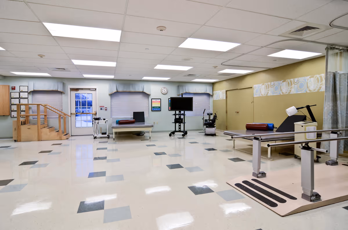 Bright rehabilitation room with a therapy bed, exercise equipment, and a stair setup.